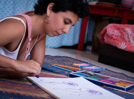 Creative Young Woman Using Pastels on Living Room Floor at Home Creative Young Woman Using Pastels on Living Room Floor at Home